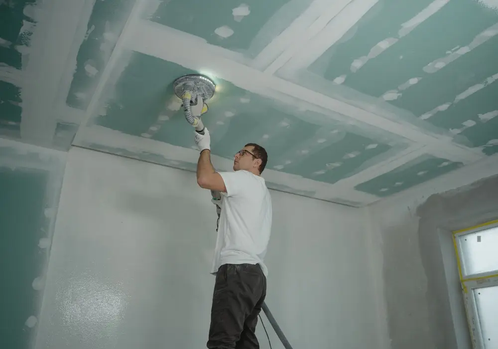 Worker sanding new ceiling drywall